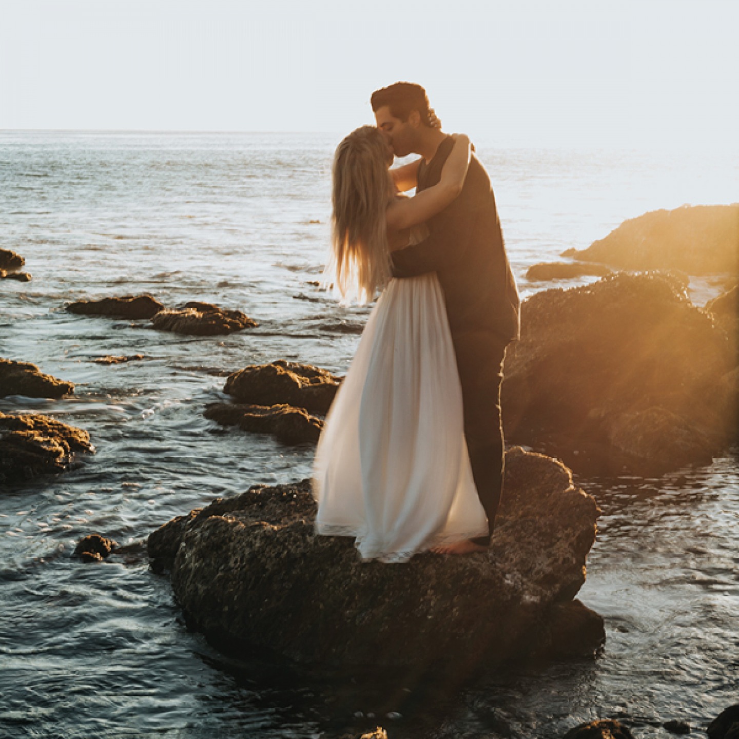 Bride and groom kissing on a rock in the ocean