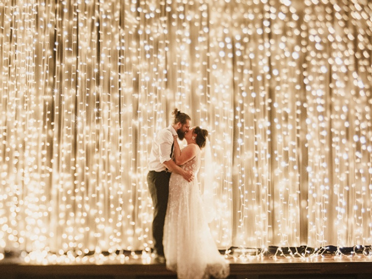 Alex and Dan embracing in front of a curtain of fairy lights