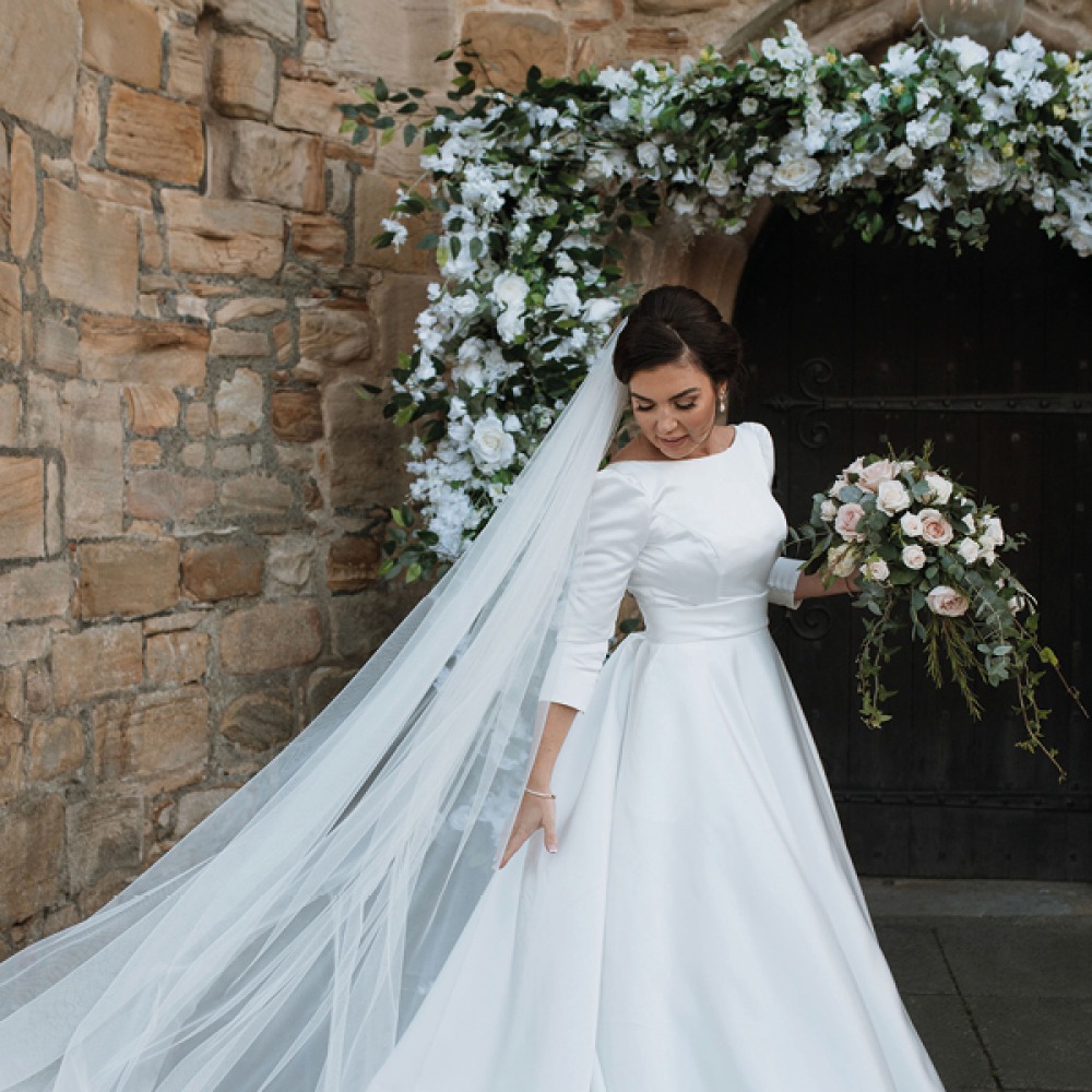 bride with bouquet and floral arch behind her