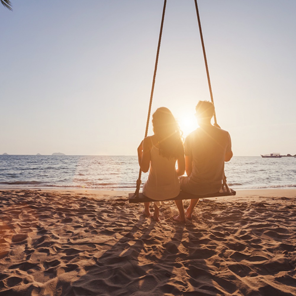 Couple on a beach swing watching sunset