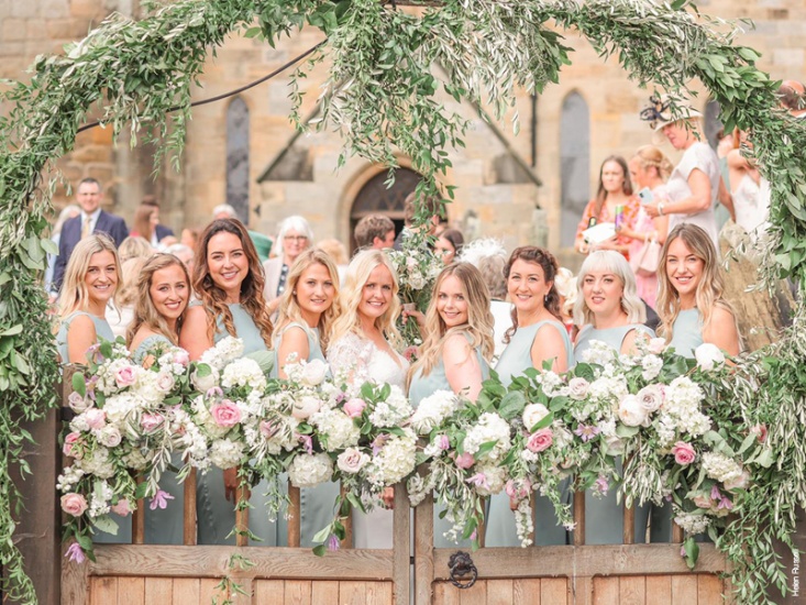 Bride and Bridesmaid posing with their bouquets under gate arch