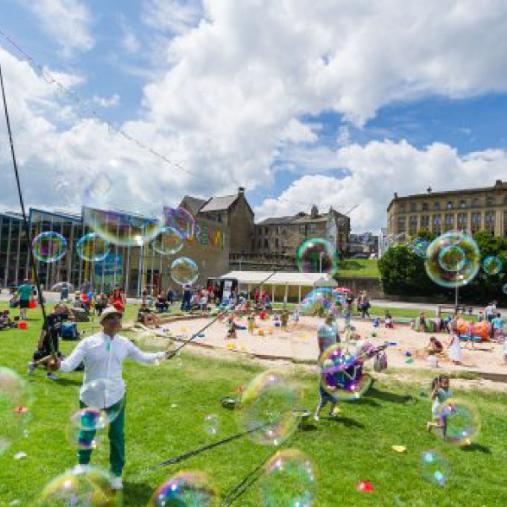 Children playing and a man making giant bubbles outside at Eureka! The National Children’s Museum