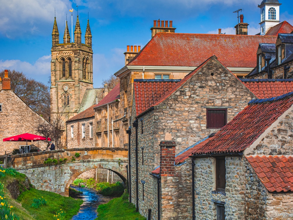 stone buildings with red tiled roofs, stone bridge over a river with a church in the background