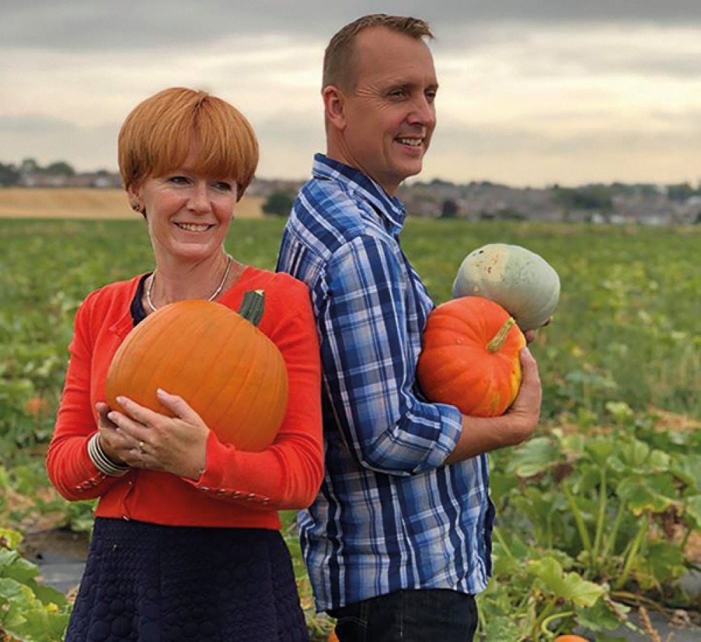 man and woman holding pumpkins in a pumpkin field