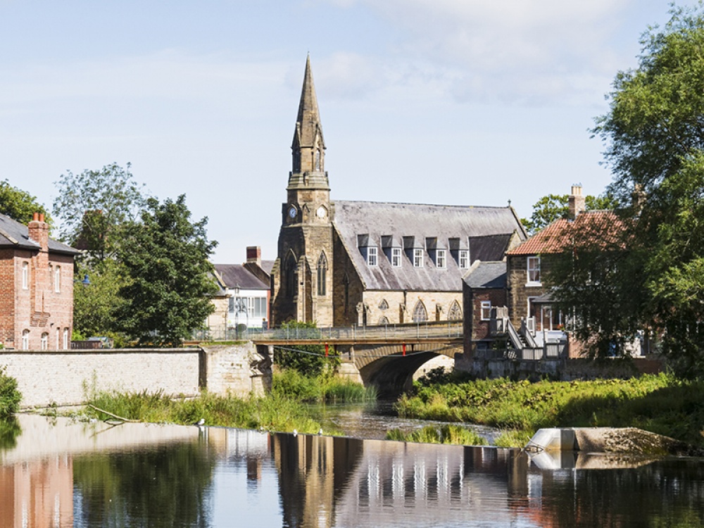 River with grassy hill, bridge and church in the background