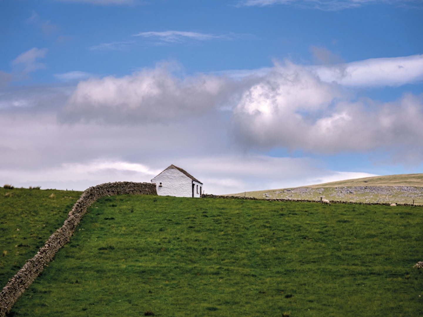 White building sitting in a field with dry stone wall