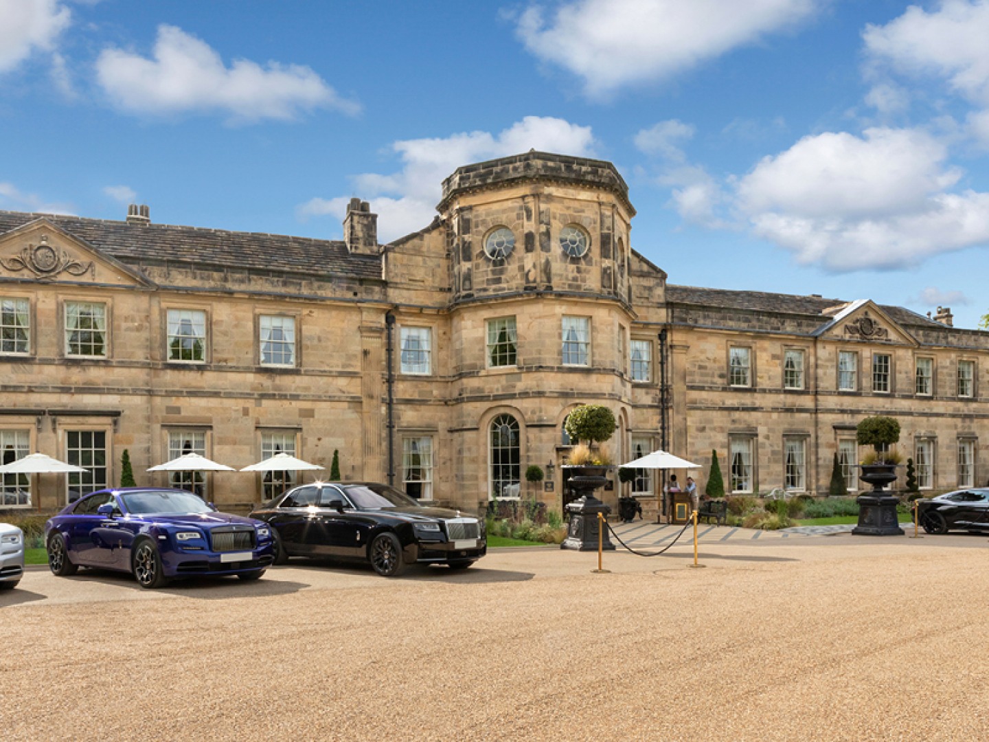 cars parked outside a grand old building, which is now a hotel on a summers day