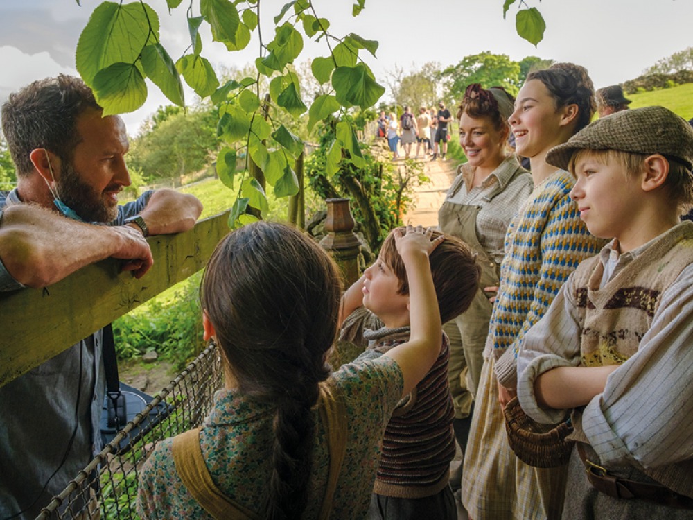 various members of the cast chatting with the director over a fence on set