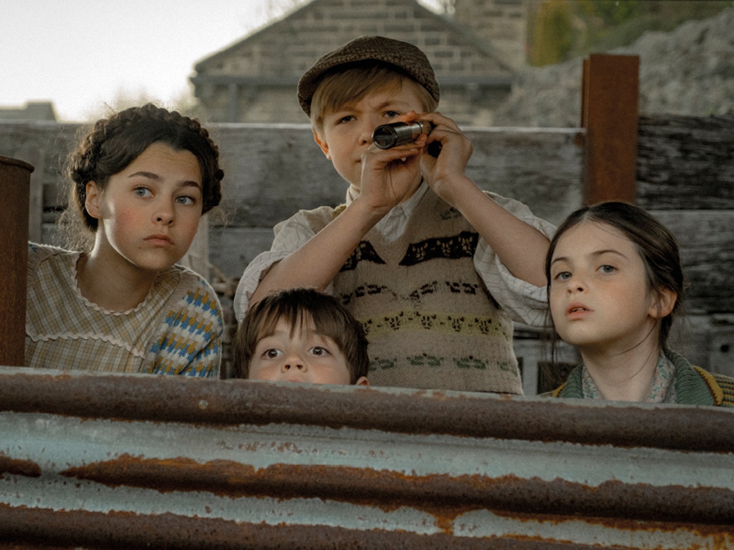 4 children hiding behind a fence watching over