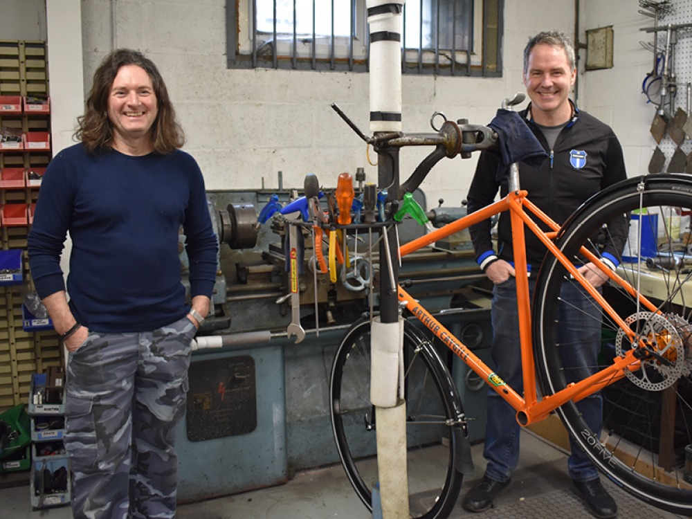 2 mens standing with a bike frame