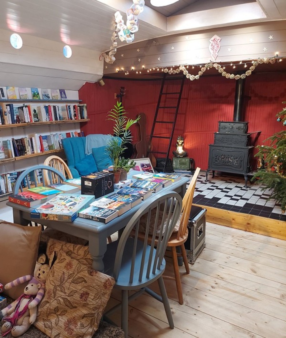 small book shop with books stacked on a blue table with a fire behind