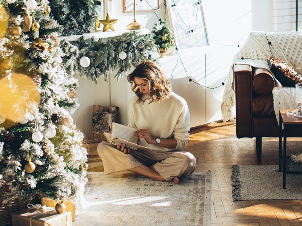 lady read a book underneath a Christmas tree