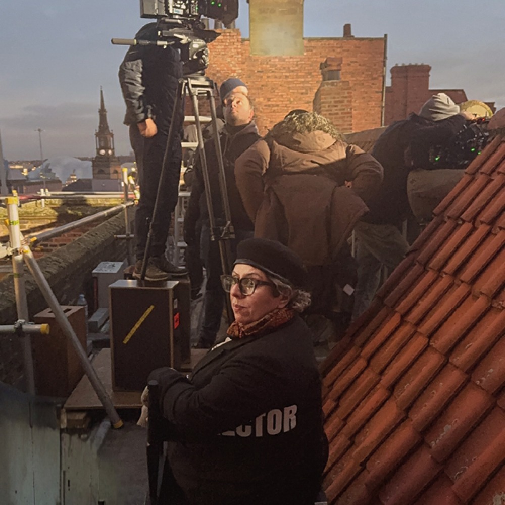 Tina Gharavi sitting in the directors chair while filming on a rooftop