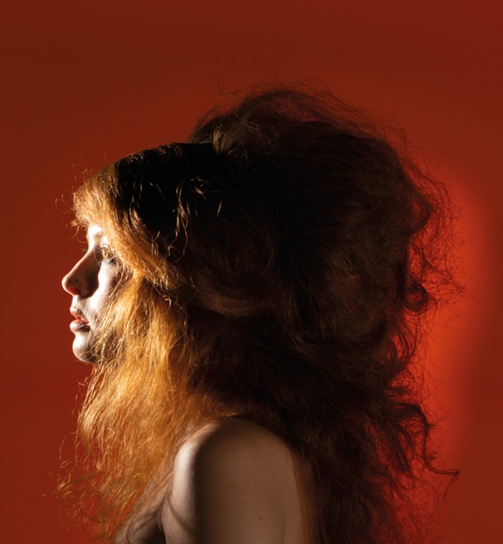 side portrait of a woman with styled red hair on burnt orange background