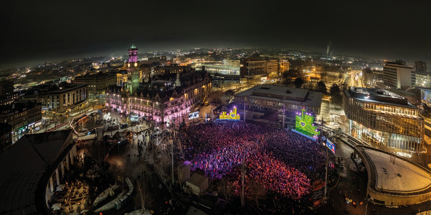 Aerial shot of RISE taken by drone, showing the crowd, the staging, and the City Hall lit up in Bradford 2025 colours © Bradford 2025