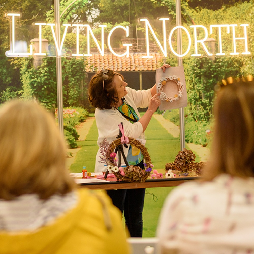 a women demonstrating how to make a wreath infant of a neon sign which reads Living North
