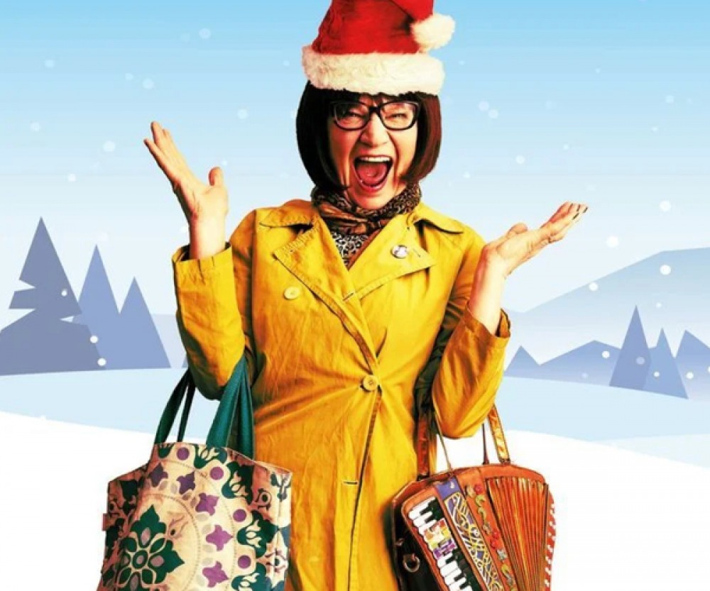 woman with a yellow coat and a Santa hat, with hands up smiling