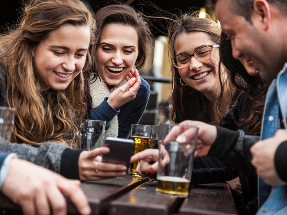 Group of people sat around a table with drinks looking at a mobile phone