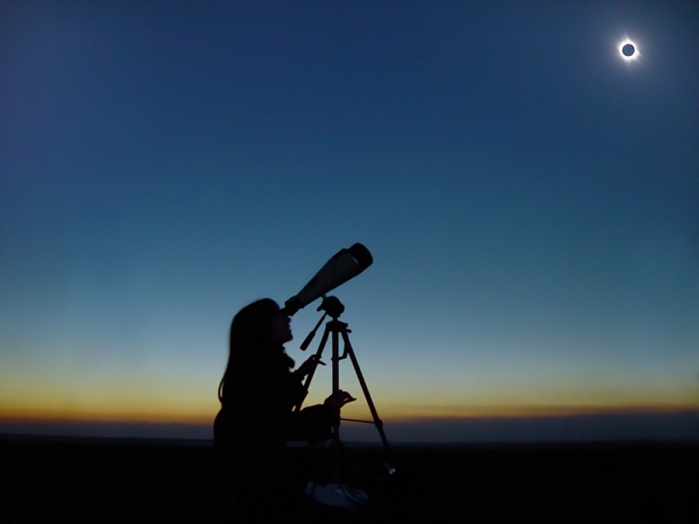 silhouette of a person looking through a telescope at the eclipse 