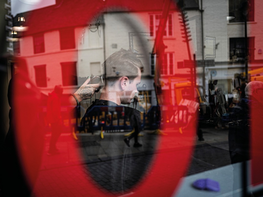 Saddler Street, Durham: a view through the window of Bronx Barbershop, showing a man getting his hair cut.  Bronx Barbershop, 67 Saddler Street, Durham. Photographer: Carl Joyce