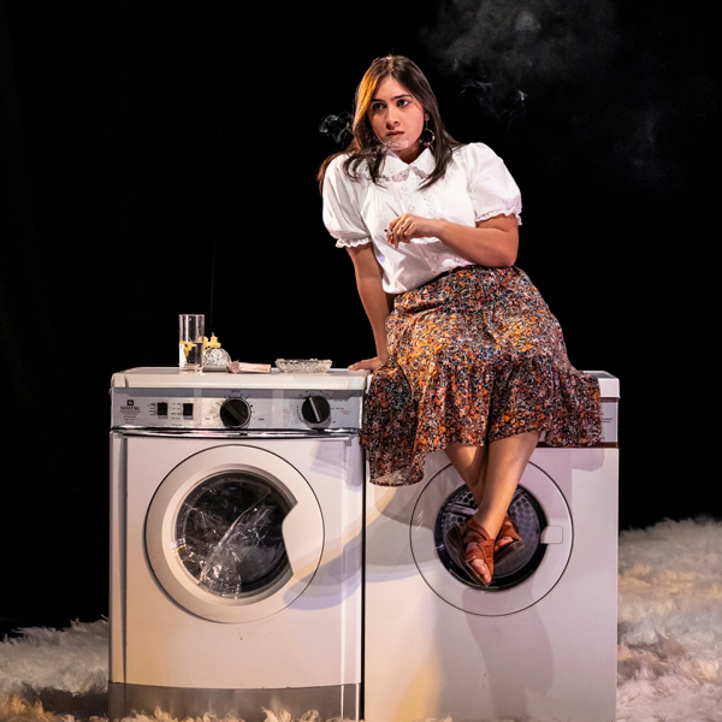 female cast member sitting on a washing machine smoking