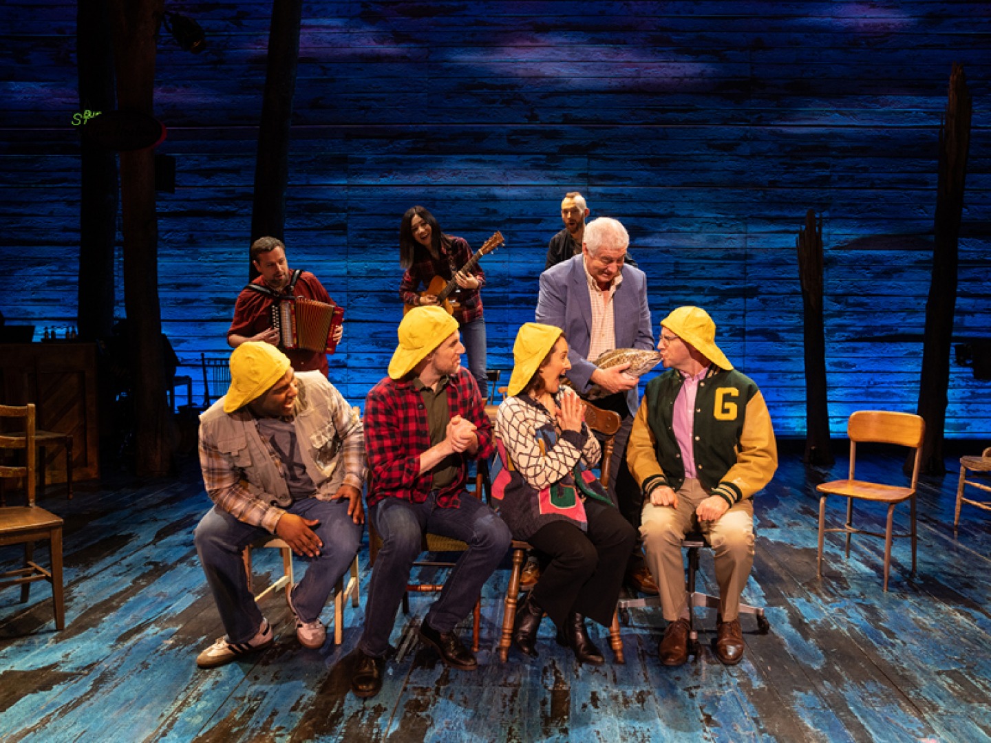 members of the cast sitting on stage wearing yellow hats