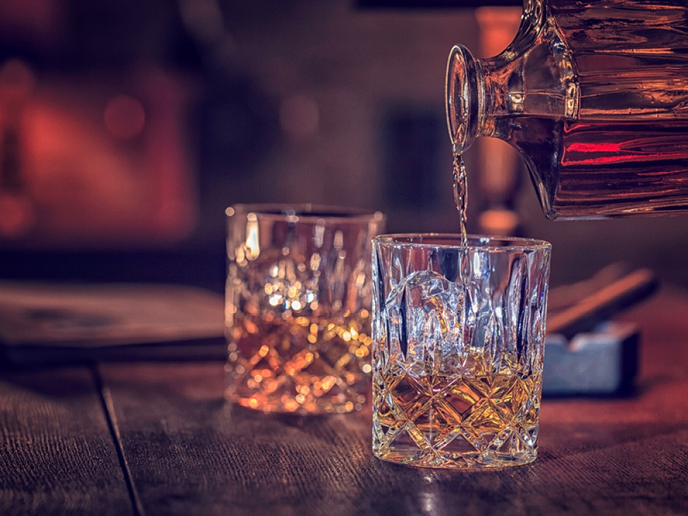 whiskey pouring from a cut glass decanter into cut glass tumblers
