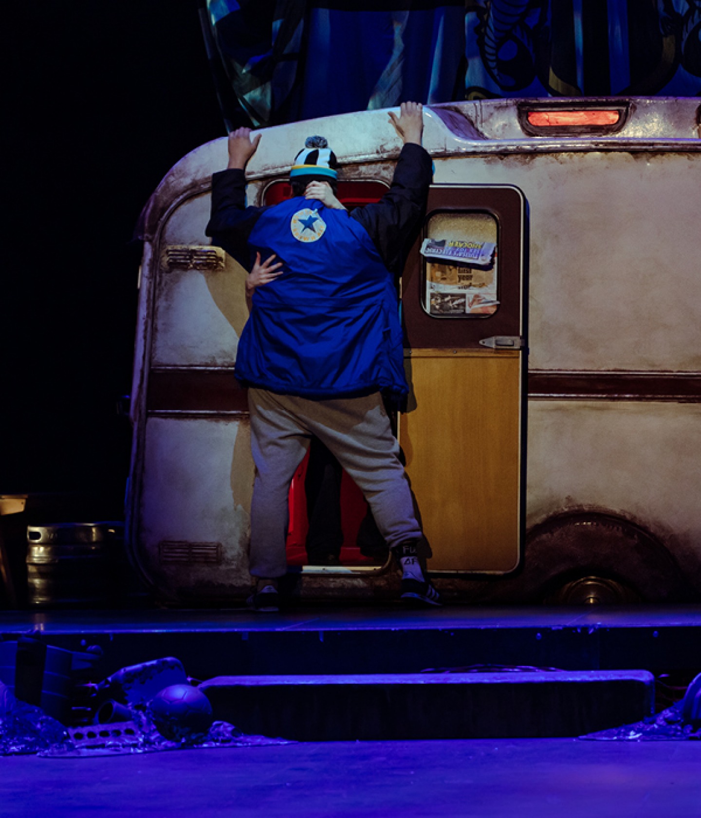 Sewell standing over a open caravan door being embraced by another cast member