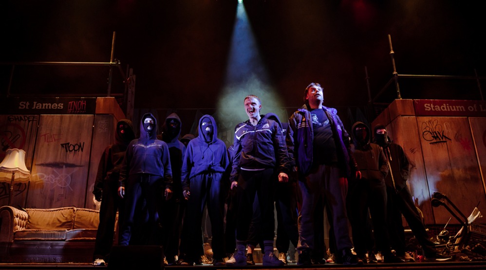 Cast members on stage dressed in black wearing balaclava