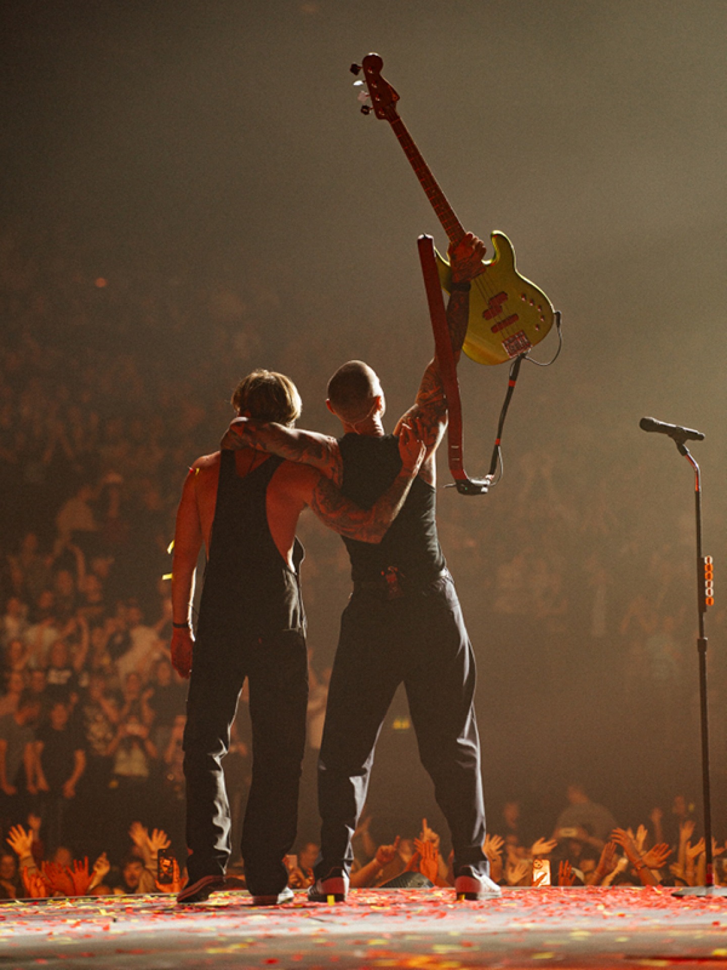 2 member of Mcfly and Busted holding a guitar in the air looking out from the stage over the crowd