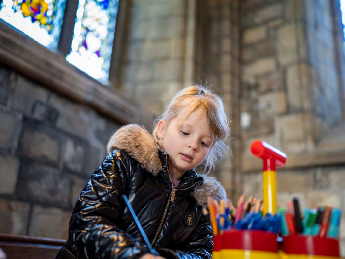 a child wearing a black coat drawing in a church