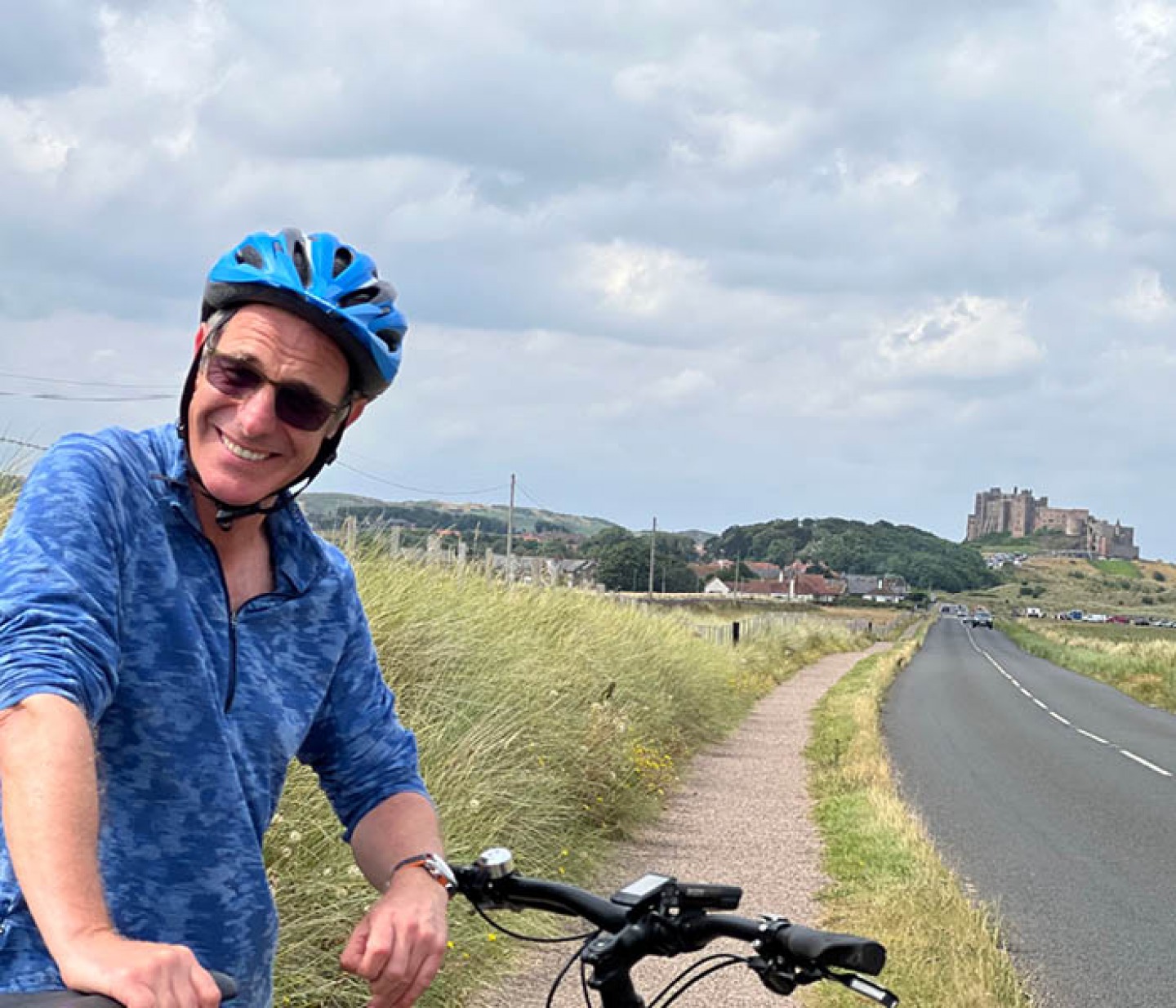 Robson Green standing with his bike near Bamburgh Castle