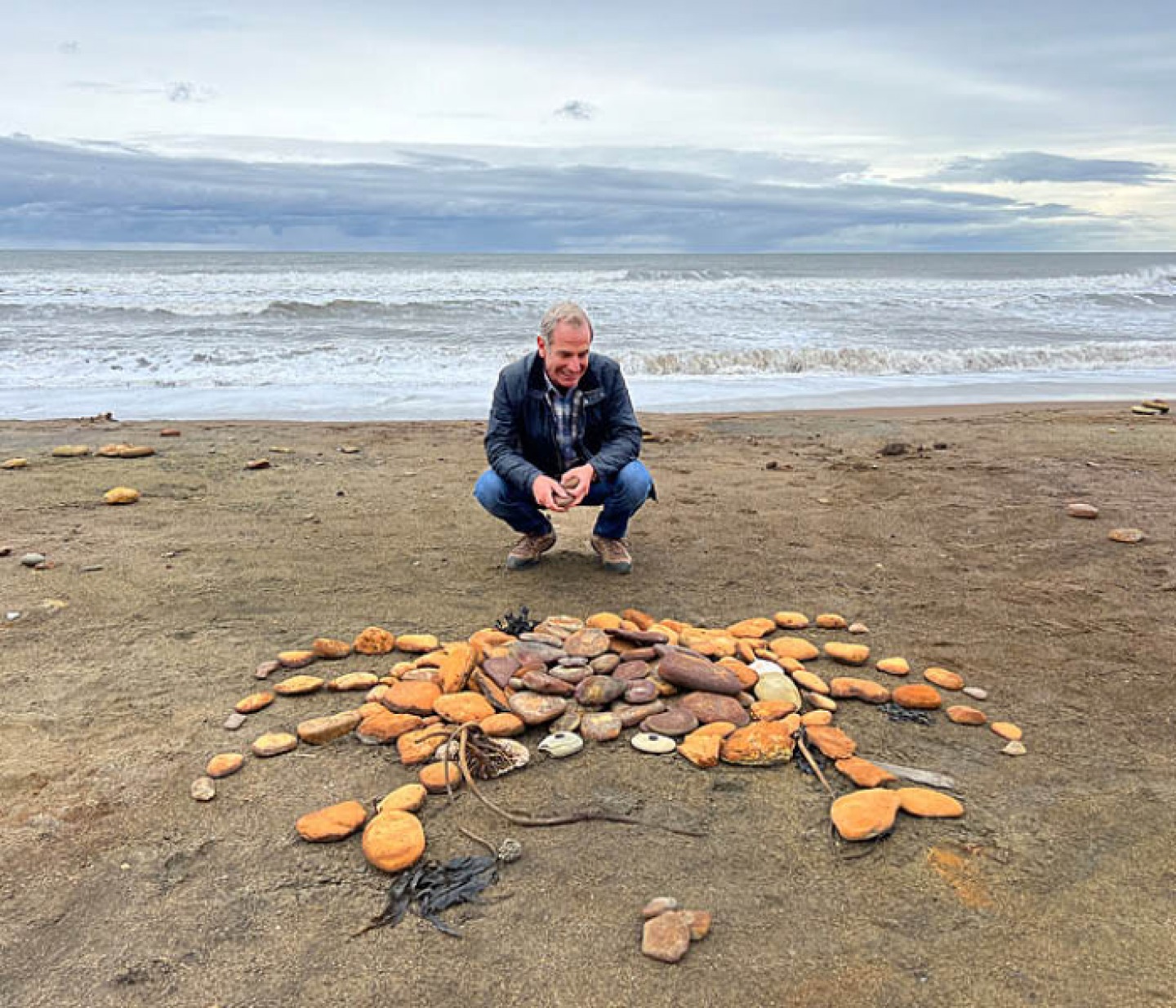 Robson Green on a beach behind a crab mural made of stones