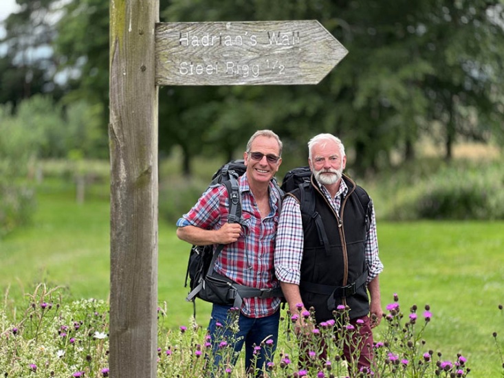 Robson Green stood with a man in front of a sign post for Hadrians Wall