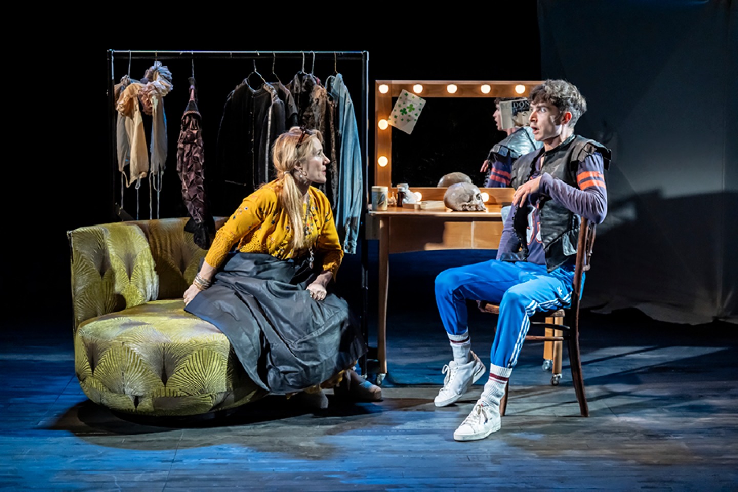Set of a dressing room with a woman sitting on a couch and a young man sitting in front of a vanity mirror
