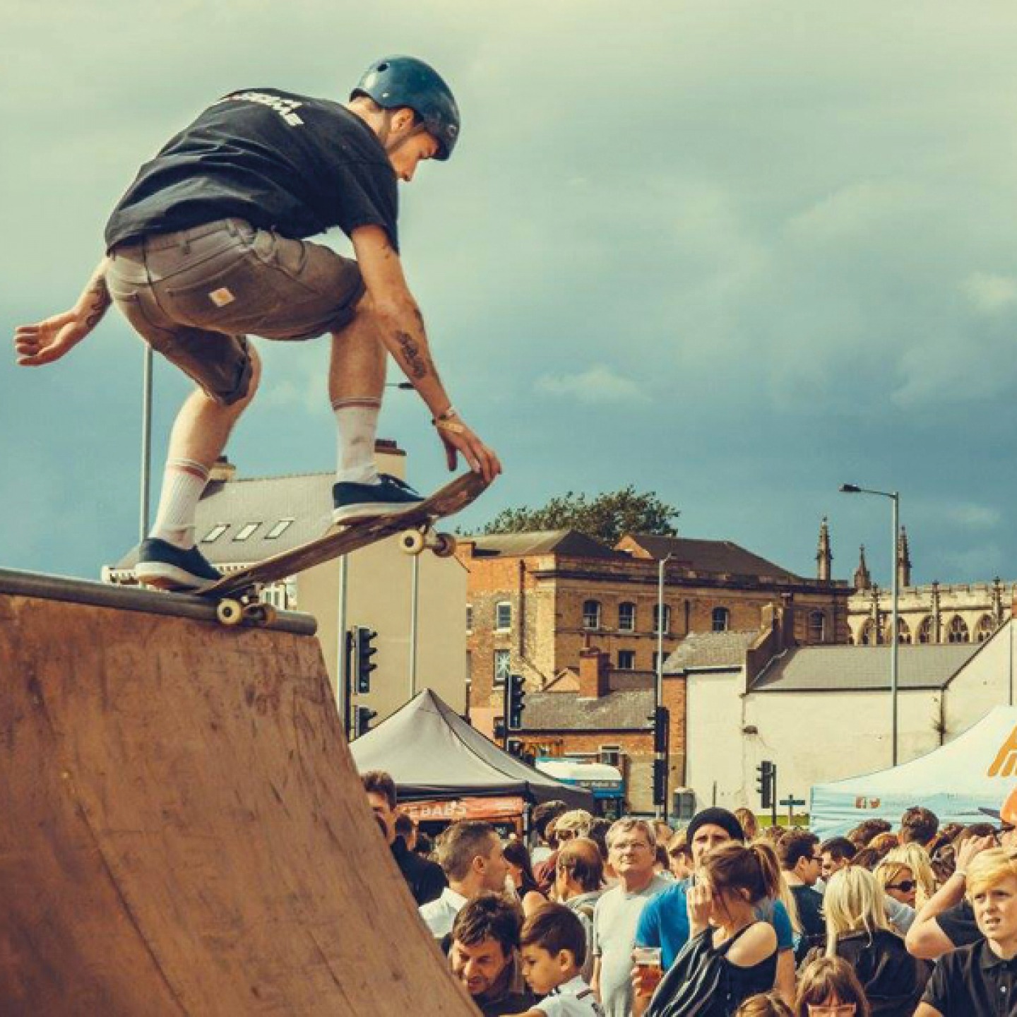 skateboarder on the edge of a half pipe with festival goers in the background
