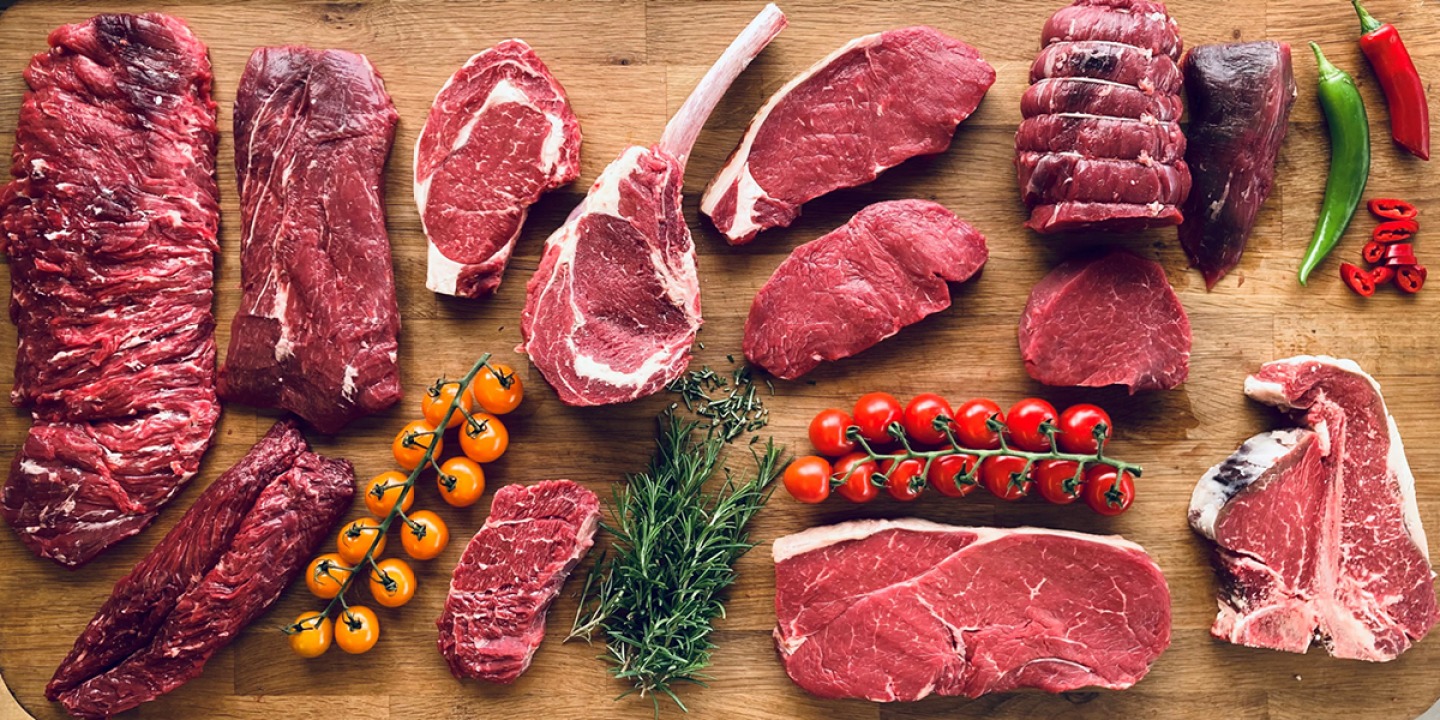 Large board of different cuts of meat stayed with vine tomatoes chillies and herbs
