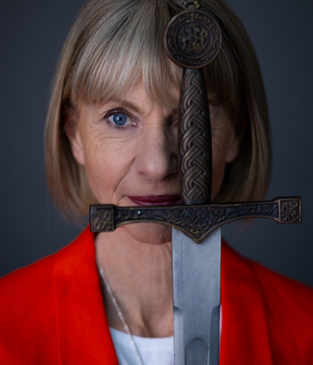Kate Mosse with the handle of a sword covering one eye and the blade pointing down