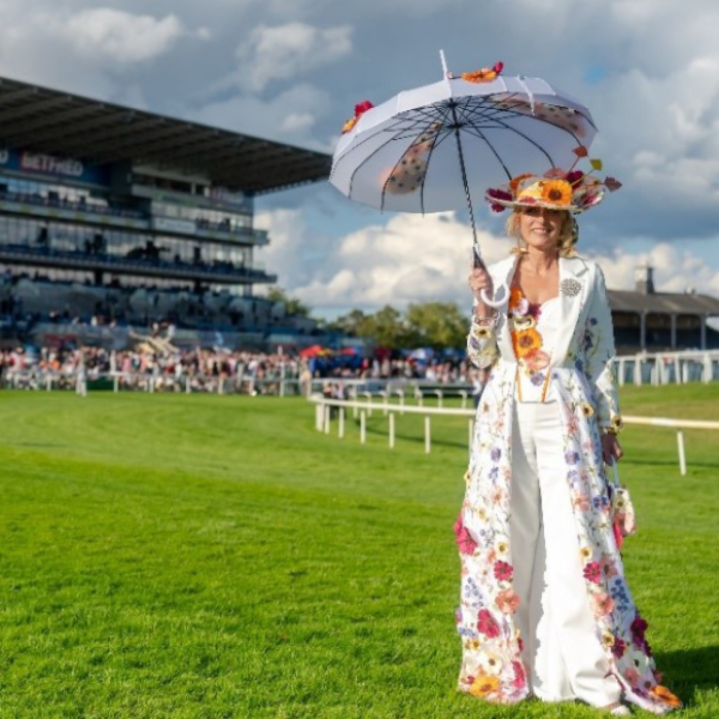 Lady dress in a long white fitted coat embellished with flowers holding a sun umbrella to match